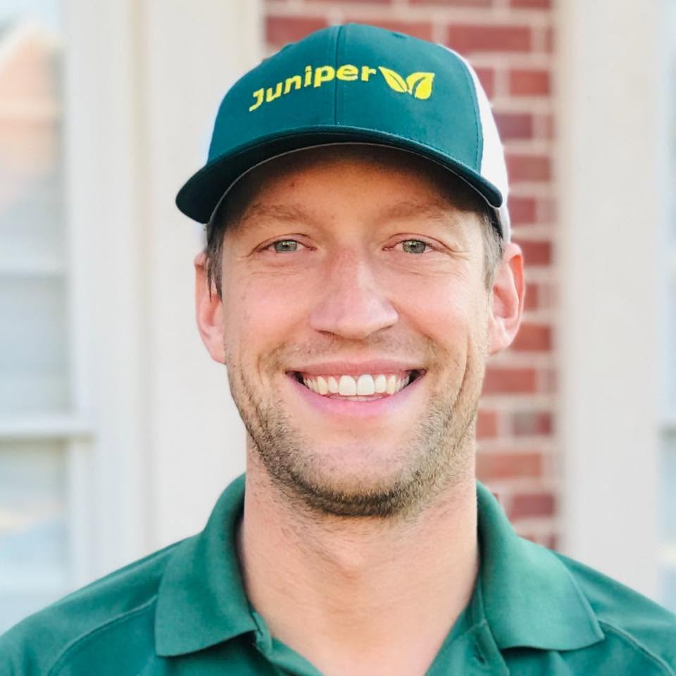 Mike wearing a Juniper cap and green work shirt outside a brick home